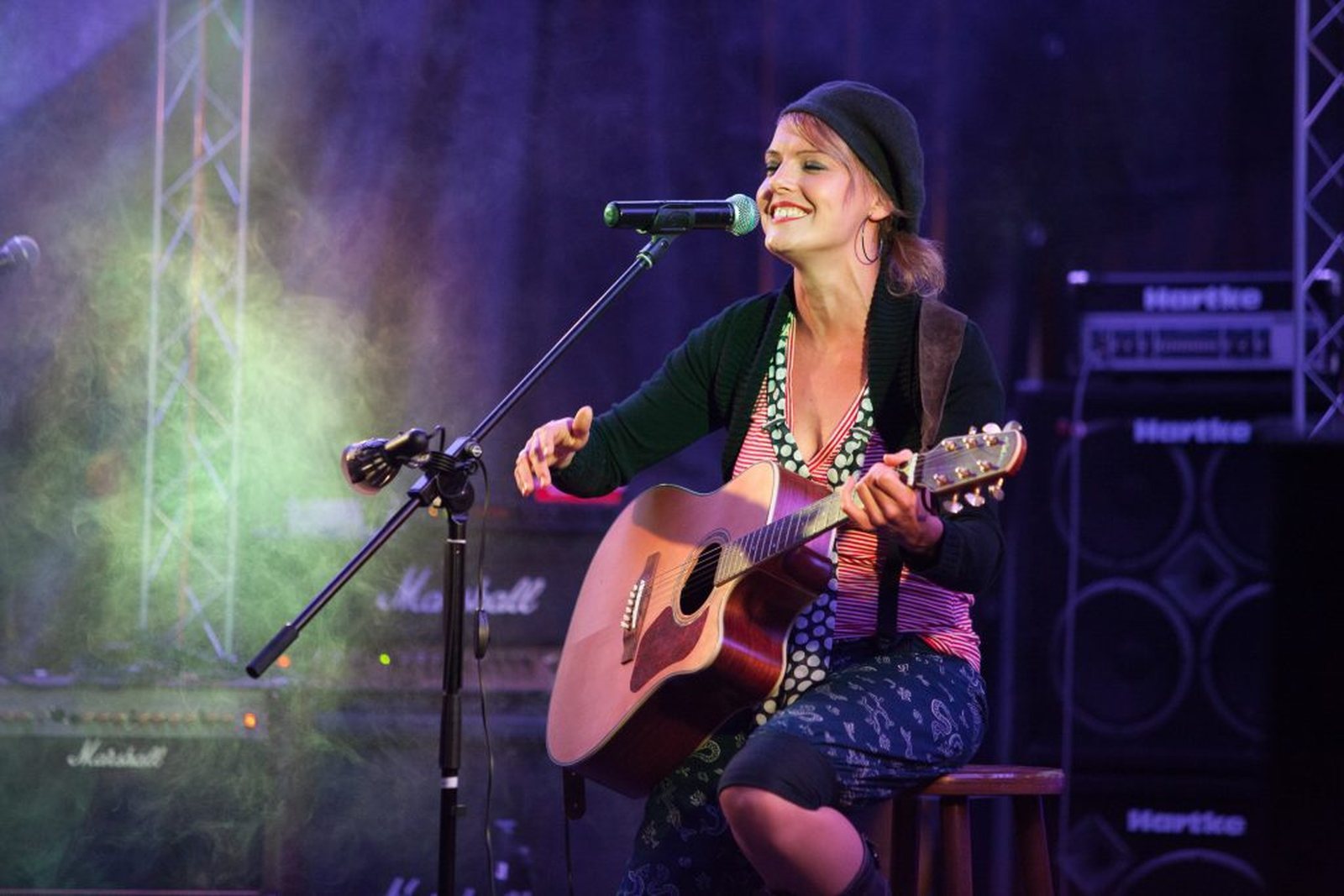 Sanni Kellermann von Sanitorium singt lachend mit akustischer Gitarre am Mikrofon auf der Bühne