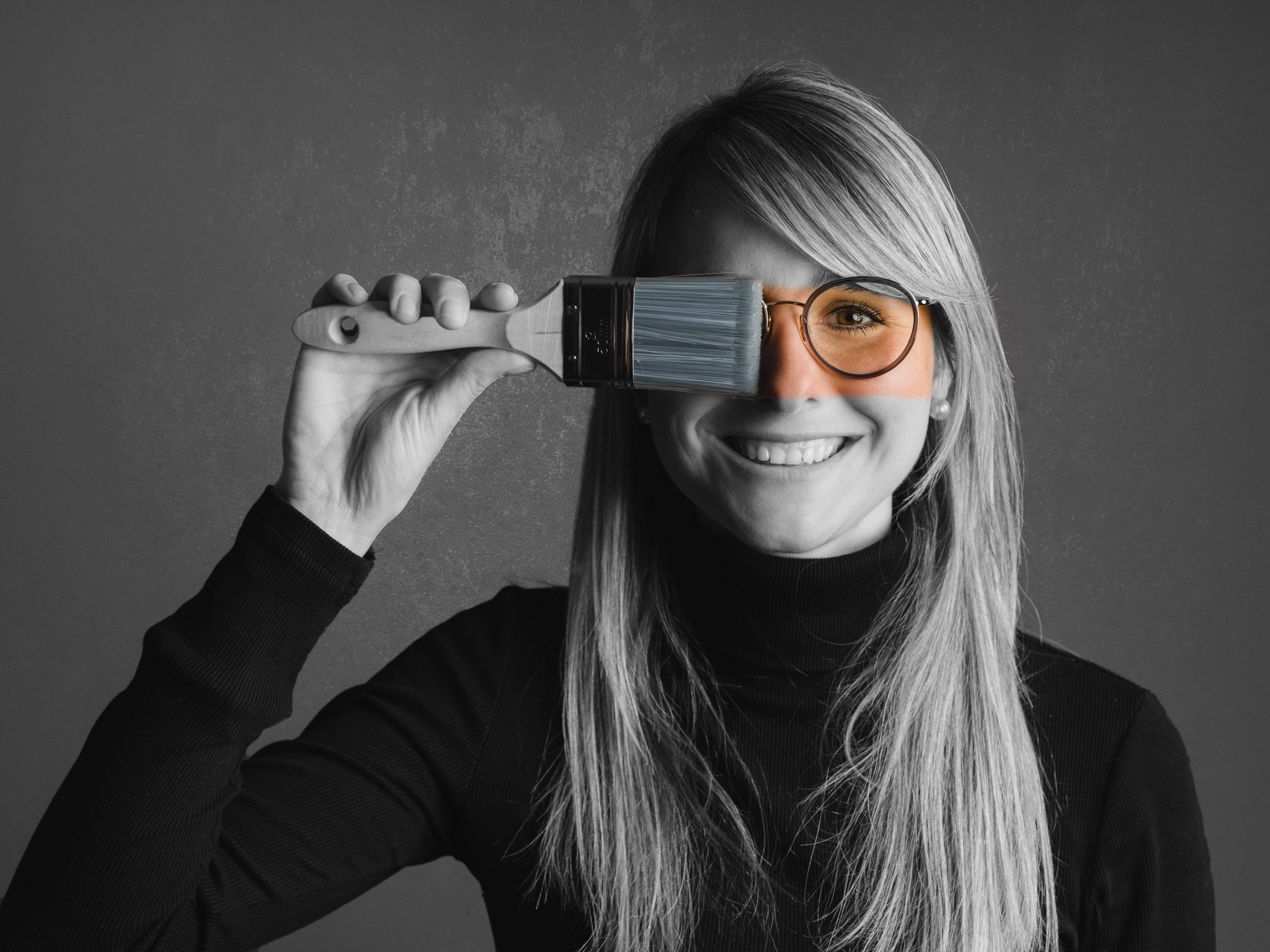 Portraitaufnahme einer Frau mit Pinsel vor dem Auge, Studio in Schwarzweiß mit Farbakzent